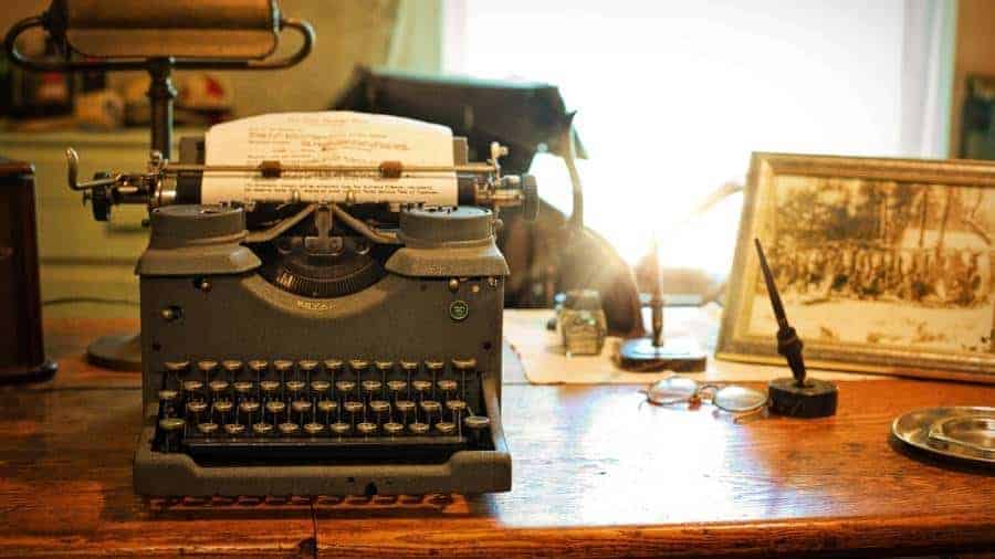 A writer's wooden desk with an old-timey typewriter and a black-and-white photo in the background. 