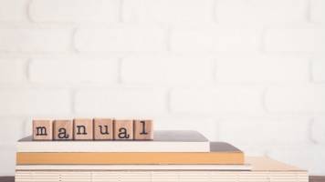 Atop several books are wooden block letters that spell out the word manual. 